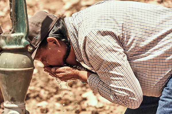 A person bends down to drink water from a water pump on this very dry land 