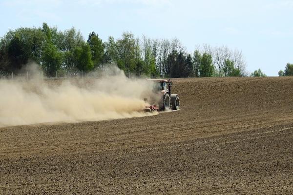 A tractor drives across barren agricultural land and kicks up dust behind it
