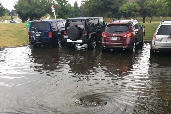 A parking lot is flooded with rainwater and four parked cars. 