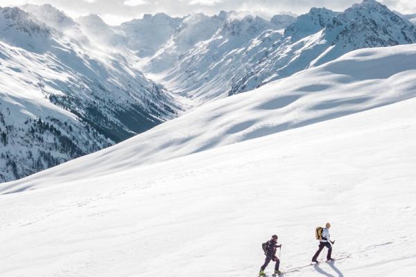 Two mountain climbers ascending on a sunny day with snow covered mountains.