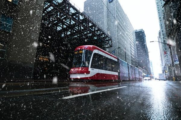A red streetcar on a city street in the rain surrounded by tall and short buildings.