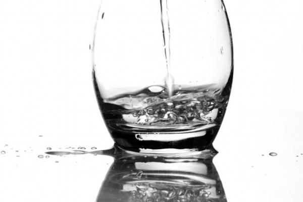 water streaming into a short Glass cup with a white background and cup reflection visible