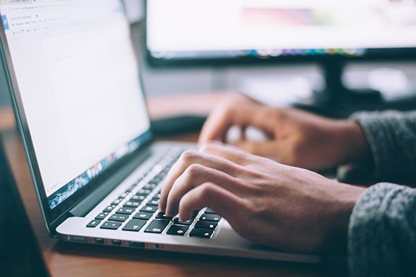 stock photo of two hands typing on computer. The screen of the computer is bright white. 