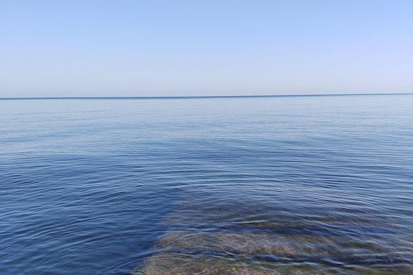 calm lake during the day with blue water and sky and silhouette of slabs of rock covered moss in forefront under water