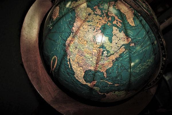 Image of partial globe focused on north America in light tan color and oceans in green on a dark wood frame with dark background