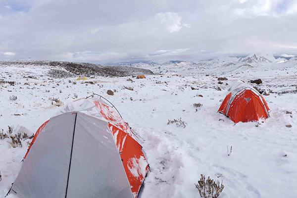 Red and gray tents in snowy research site. The landscape is snowy and rocky with gray skies.