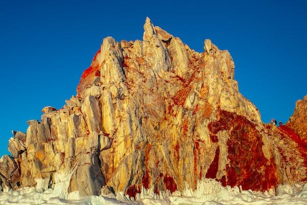 Sharman Rock in Siberia Russia yellow jagged rocky mountain with read streaks against light blue sky