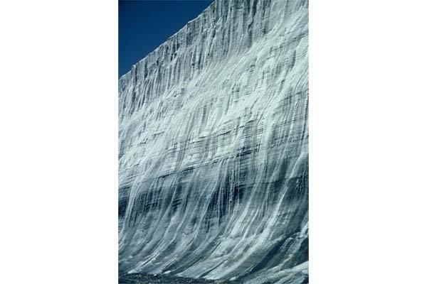 small image of a wall of ice with different layers hues of dark color with a small area of deep blue sky .