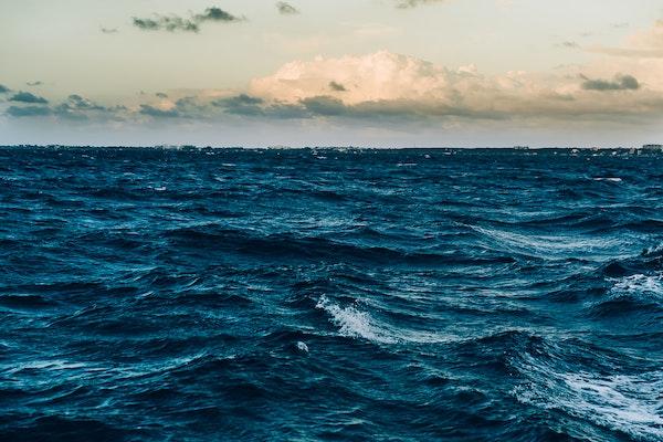 Surface view of calm open water under a white blue sky with clouds