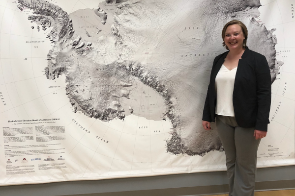 A white woman with short, blonde hair standing in front of a map of Antarctica
