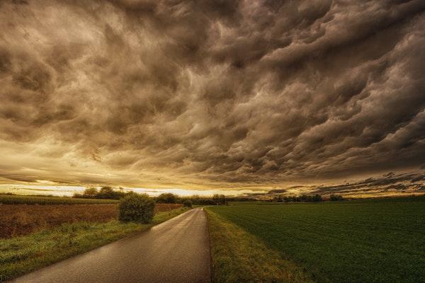 landscape of a field on either side of a road and gray sky and clouds above.