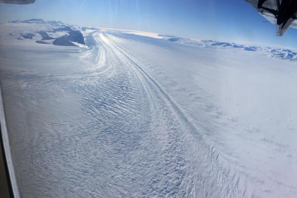 Snow covered ground from a plane with part of the plane in the right side of the image.