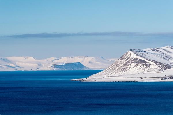 Scenic view of a body of water and snow-covered mountain and ice in blue waters under blue skies with clouds.