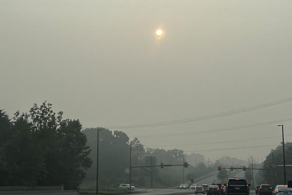 Car red taillights at a traffic light on a street in smog with haze around the sun.