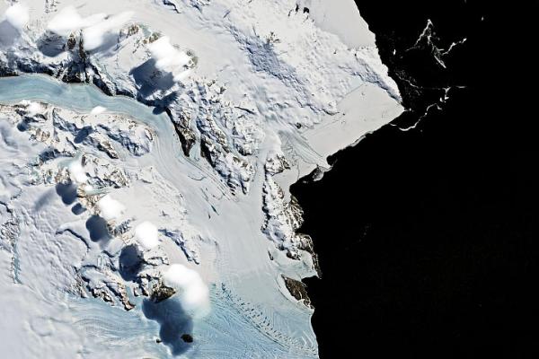 Aerial view of glaciers, snow-covered mountains and white, puffy clouds against a black background. 