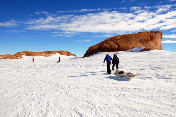 People participate in snow activities near a large sandstone rock formation under a clear blue sky.
