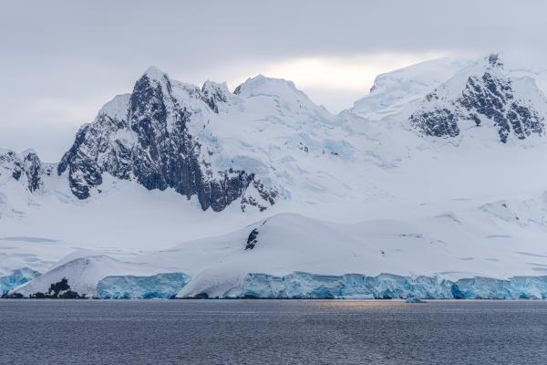 Panoramic view of Antarctica featuring expansive ice-covered mountains under a cloudy sky.