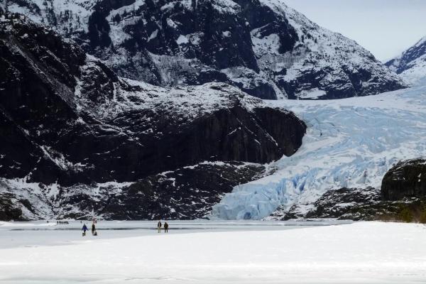People walking near a Glacier, with snow-covered mountains in the background.