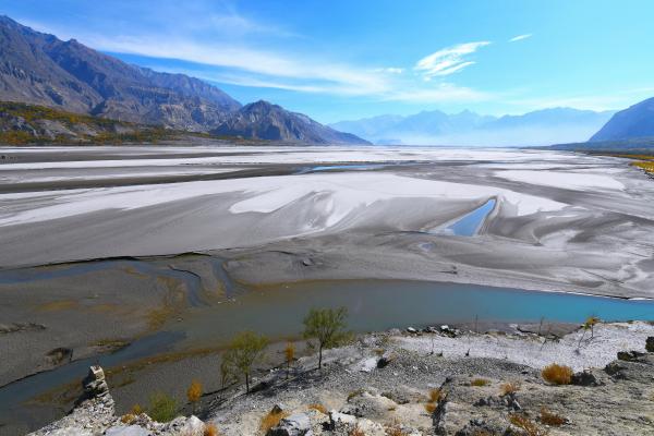 Panoramic view of a Valley showing expansive white flats, winding rivers, and distant mountains under a clear blue sky.