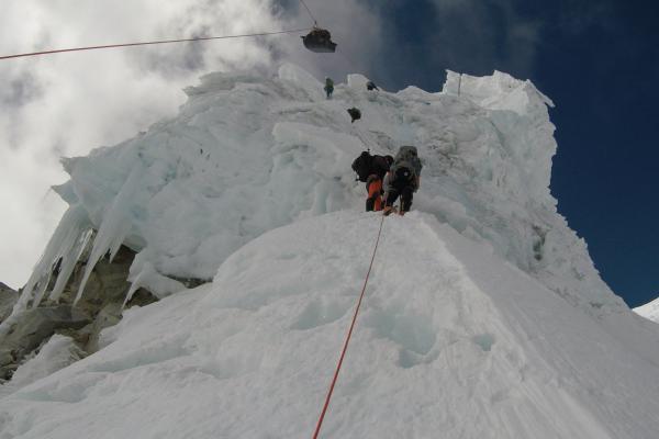 Researchers ascending a steep, icy section of a mountain and moving equipment, using fixed ropes for safety.