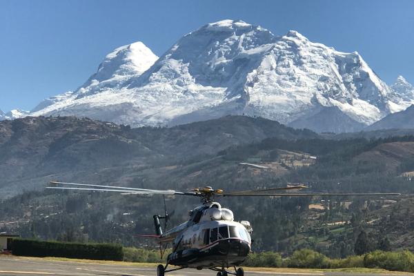 A helicopter parked on a tarmac with a mountain in the background under a clear blue sky.