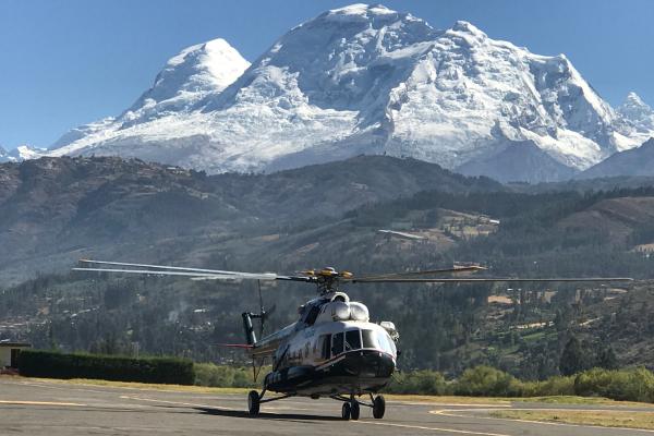 A helicopter parked on a tarmac with a mountain in the background under a clear blue sky.