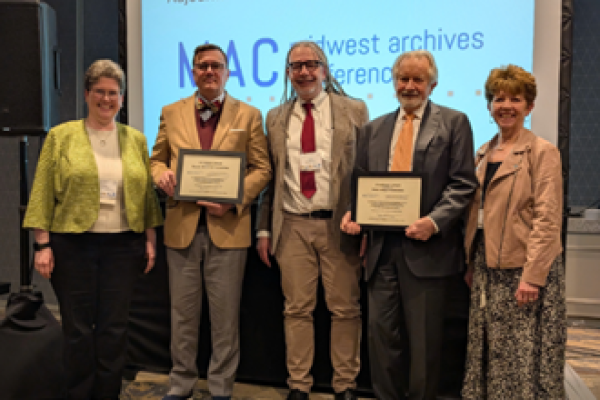 Five individuals, two holding certificates, stand in front of a presentation screen displaying "MAC Midwest Archives Conference".