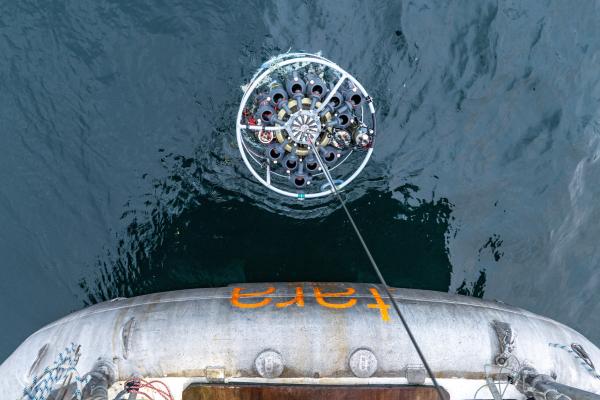 Overhead view of a circular ocean-sampling instrument array being lowered into the sea from a ship.