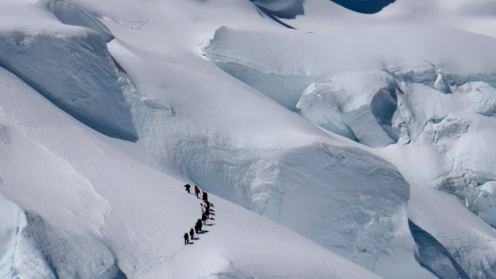 A group of researchers hiking the summit of Nevado Huascarán surrounded by snowy mountains. 