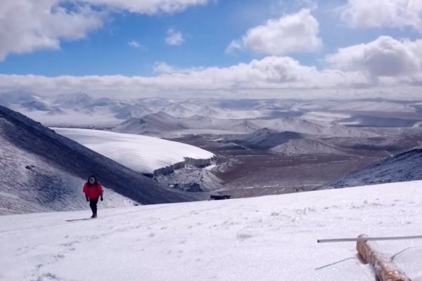 Man walking up glacier with valley and mountains