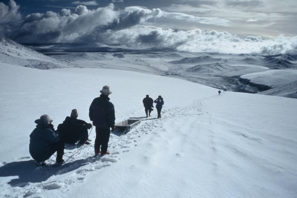 People walking on a snow covered path with a sled under gray skies.