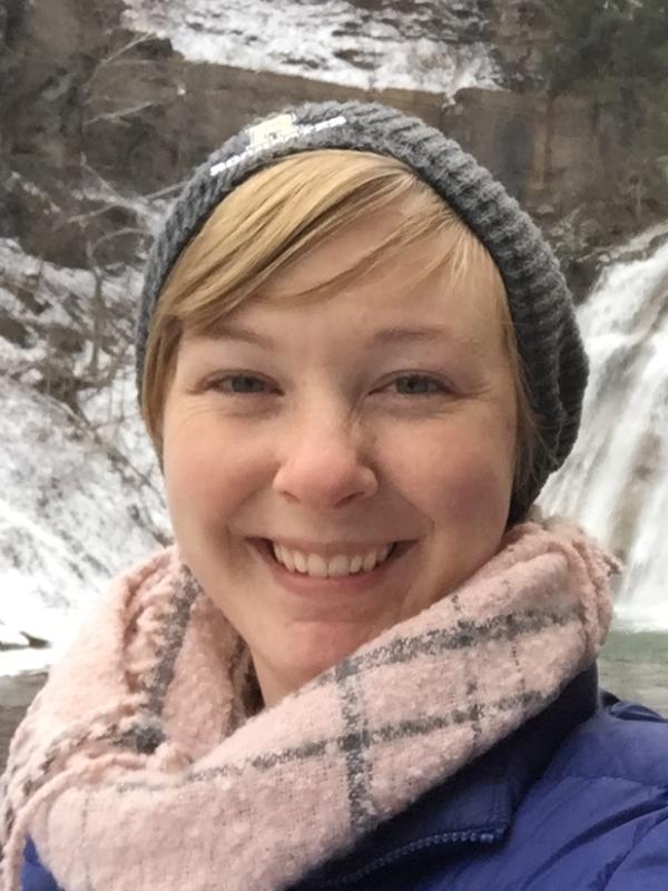 Woman in winter clothes by frozen waterfall