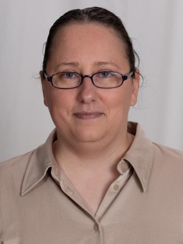 Portrait image of Iliyana Dobreva with hair pulled back, dark frame glasses and beige blouse with off white background