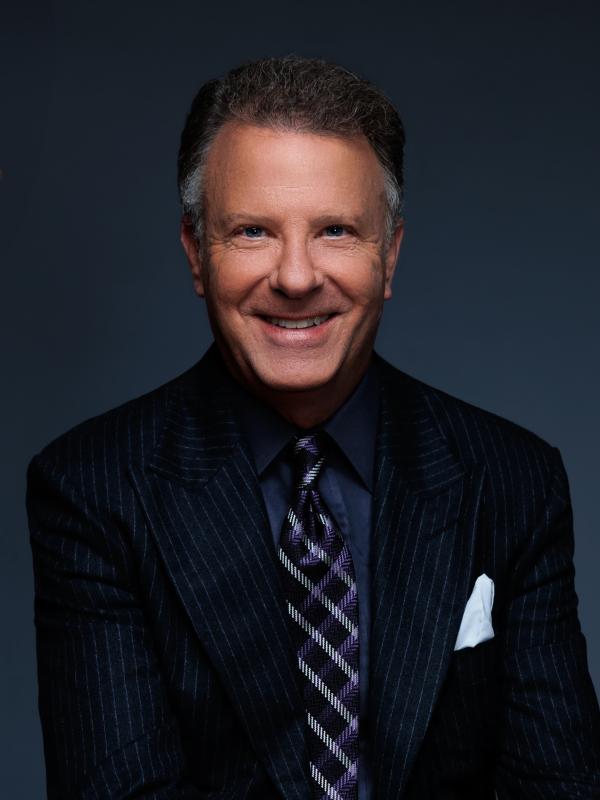 Joseph Manning wearing a suit smiling for the camera in front of a dark blue backdrop.