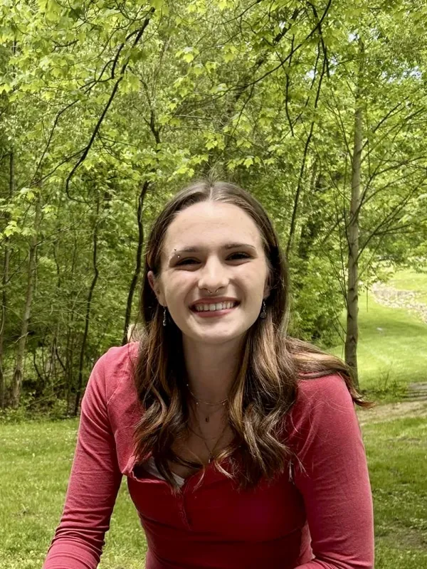 A person outdoors standing on a grassy area in from of some trees