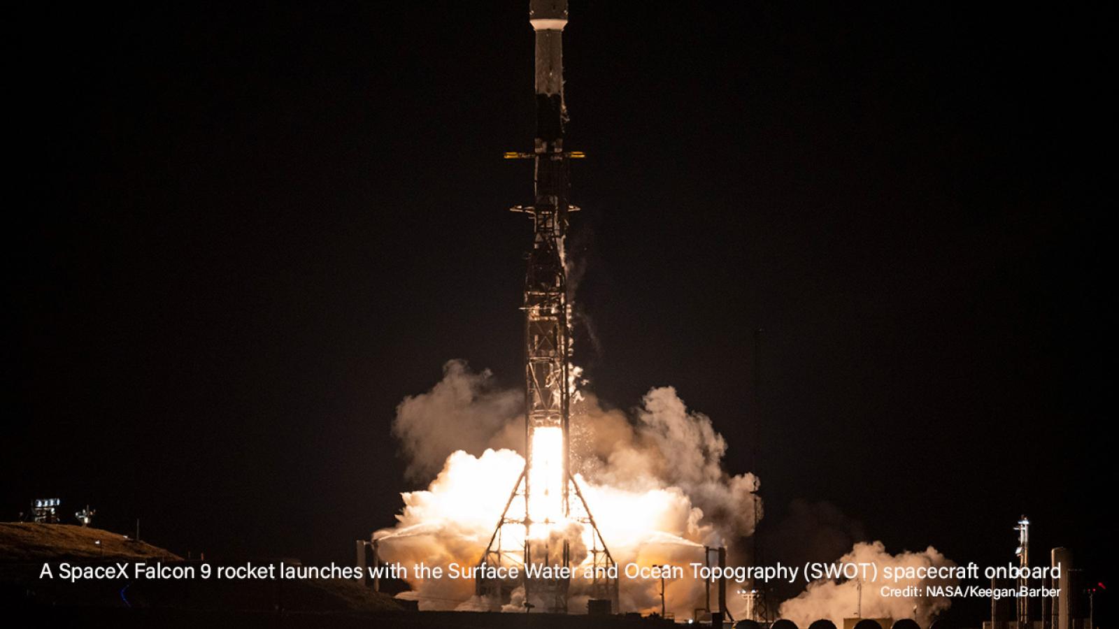 A SpaceX Falcon 9 rocket on the platform being launched in the dark with smoke and fire coming out from beneath it