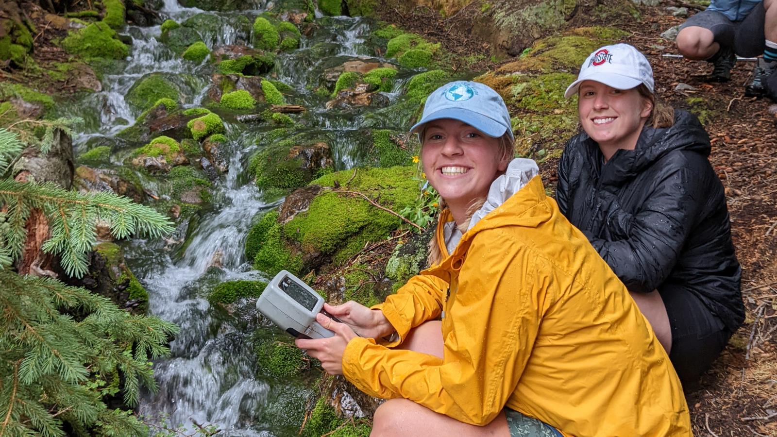 Three people crouched down next to a moss filled stream with equipment in their hands. 