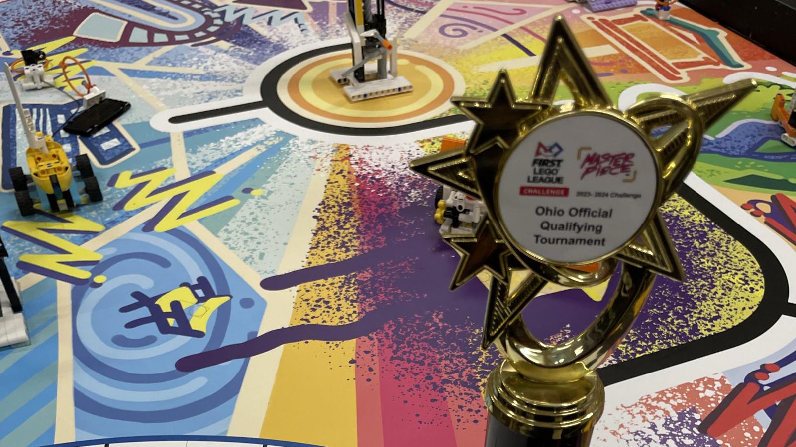 A picture of a trophy on a table with a colorful surfase and text Master Piece on it. 