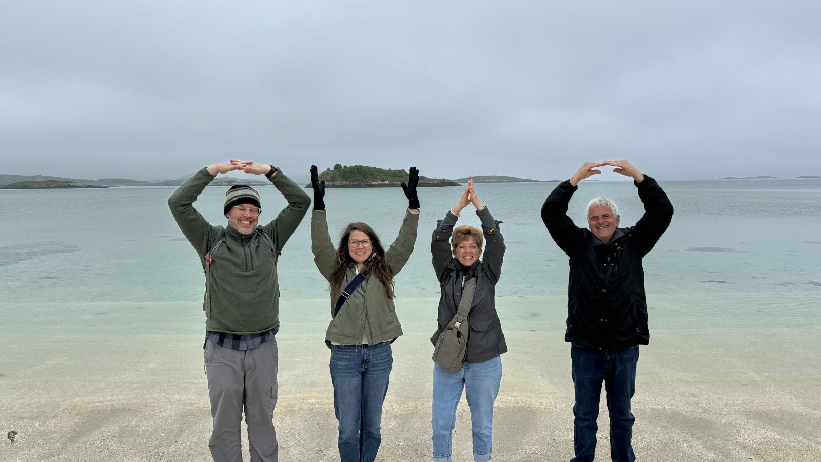 Four people standing at the beach posing spelling OHIO, each representing a letter with their arms stretched..