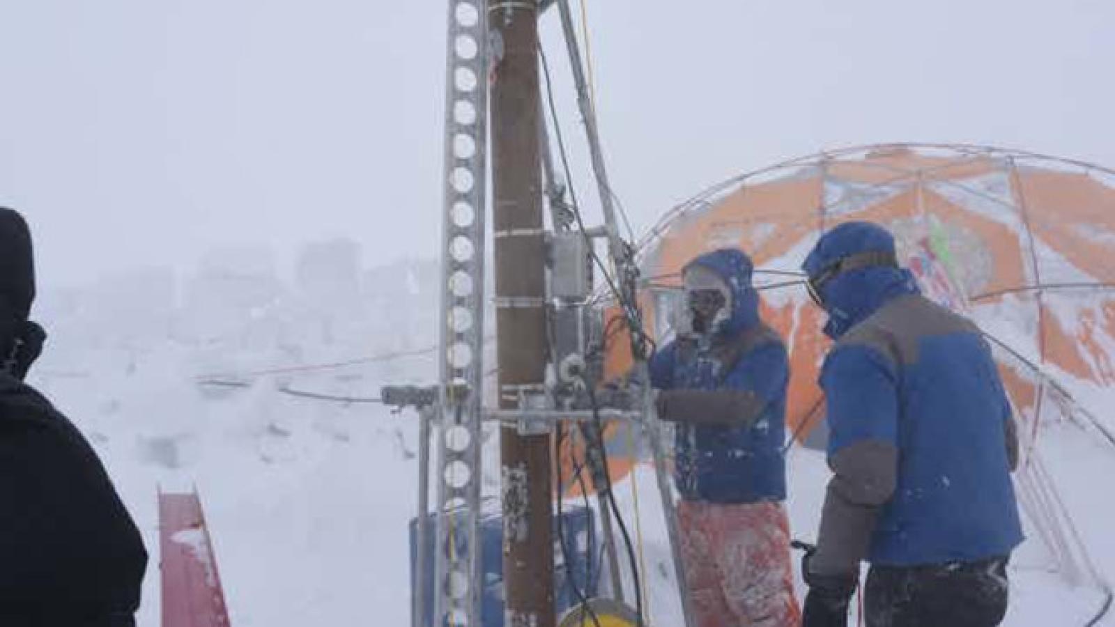People outdoors in front of an orange tent in snow working with equipment.