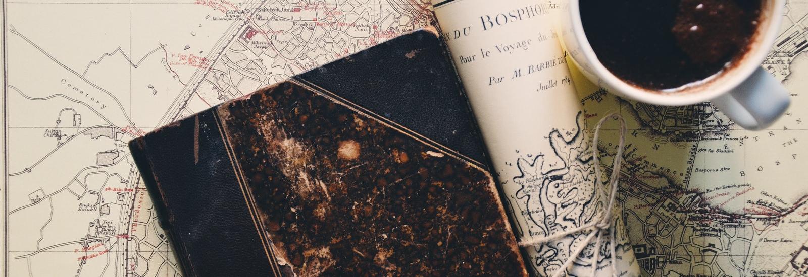 Coffee cup, rolled map and notebook on another map