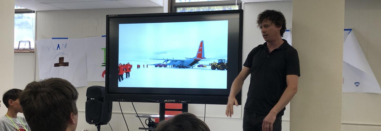 researcher presenting to students with a video display showing Antarctica.