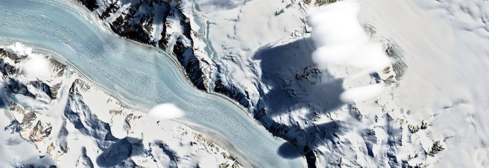 Close-up aerial view of glaciers, snow-covered mountains and white, puffy clouds.