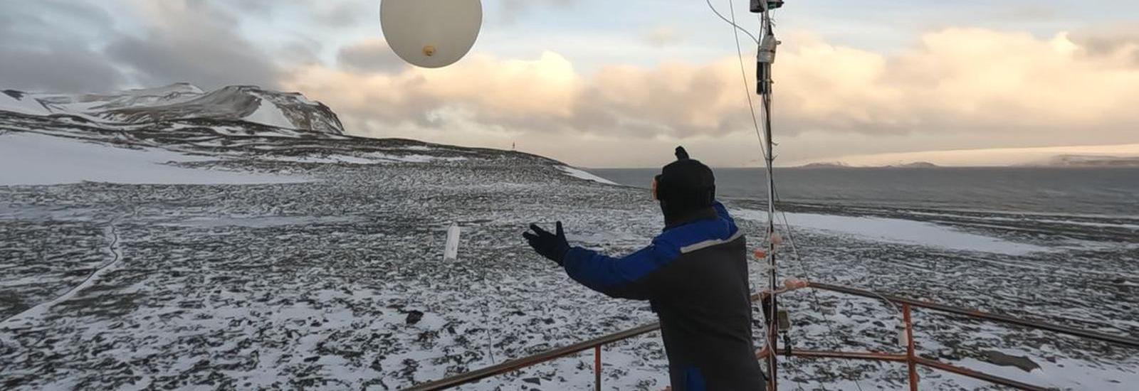 A person releasing a weather balloon into the sky from a snowy landscape during sunrise or sunset.