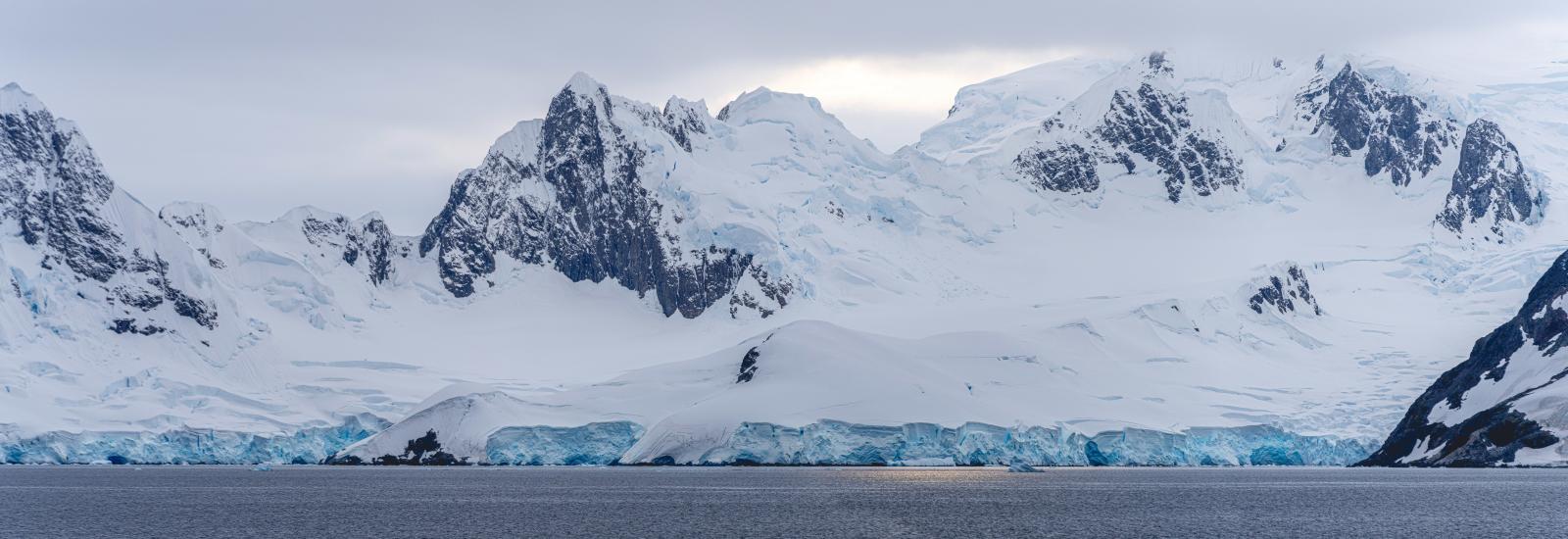 Panoramic view of Antarctica featuring expansive ice-covered mountains under a cloudy sky.
