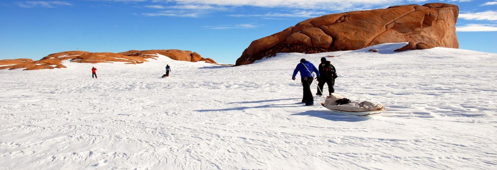 People participate in snow activities near a large sandstone rock formation under a clear blue sky.