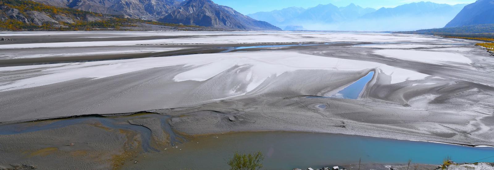 Panoramic view of a Valley showing expansive white flats, winding rivers, and distant mountains under a clear blue sky.