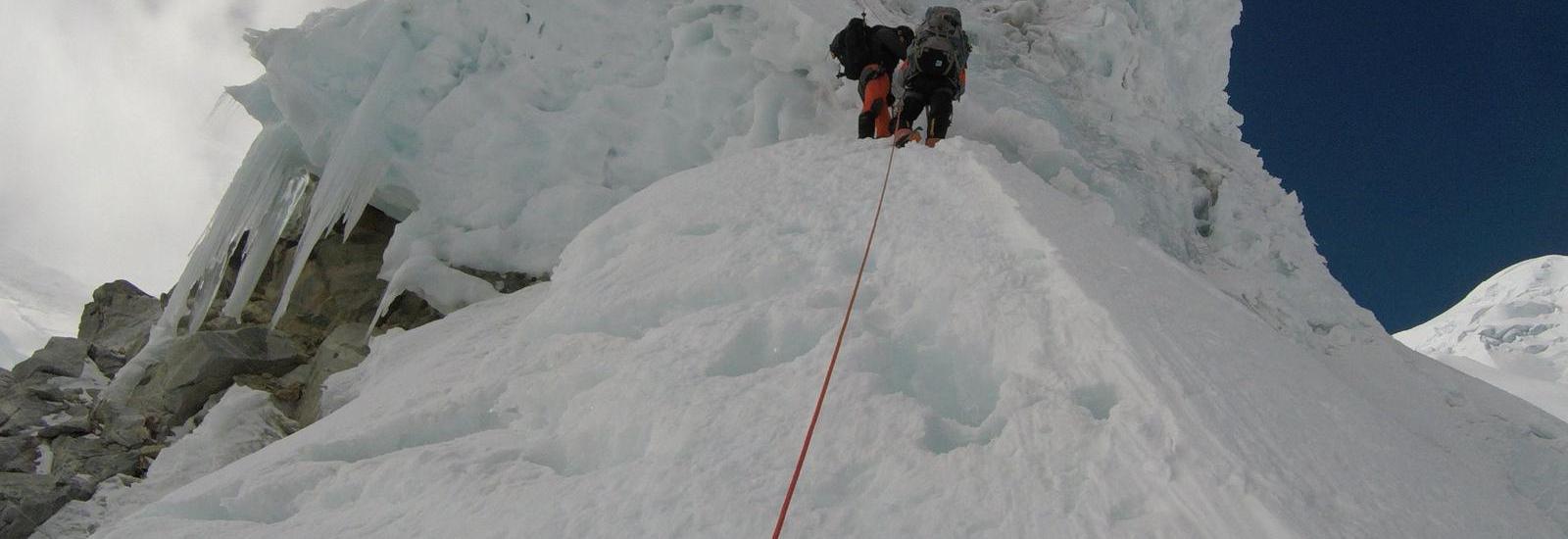 Climbers ascending a steep icy slope with a rope, under a clear sky with equipment hovering above.