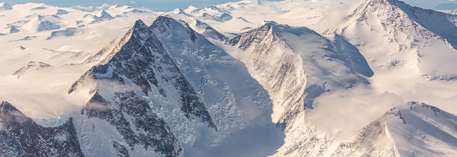 A mountain range covered in snow and ice under blue skies.