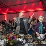 Lonnie Thompson with raised hands and Ellen Mosley Thompson standing up from a round table in a banquet hall with Georgie Shockey seated